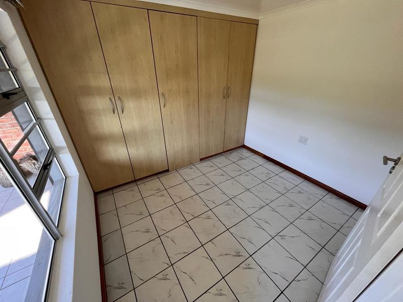 A bright, empty bedroom featuring tiled flooring and ample built-in cupboard storage, offering a clean and neutral space ready for personalization.