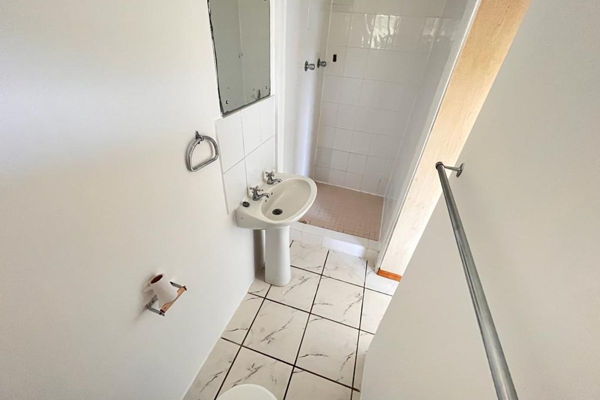 A compact bathroom featuring a pedestal basin, shower enclosure, and tiled flooring, requiring some cosmetic updates to improve its overall condition.