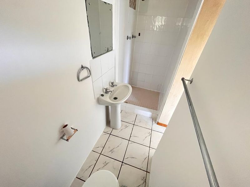 A compact bathroom featuring a pedestal basin, shower enclosure, and tiled flooring, requiring some cosmetic updates to improve its overall condition.