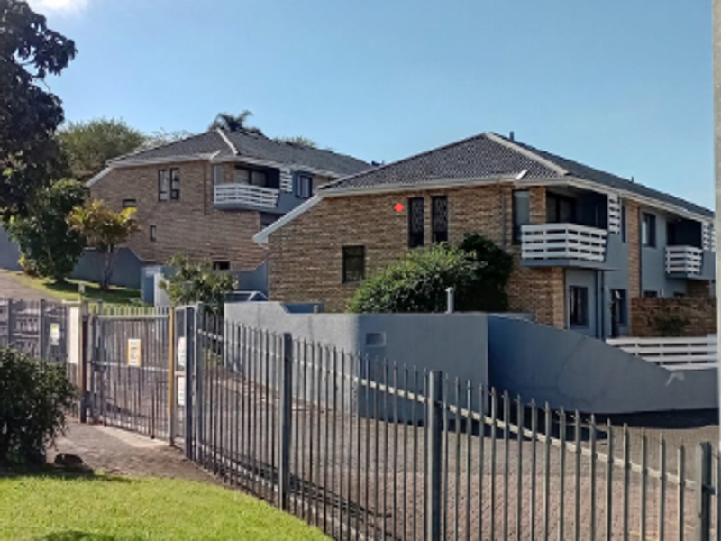 Front exterior view of a townhouse complex featuring brick facades, tiled roofs, and secure gated access with paved driveway.