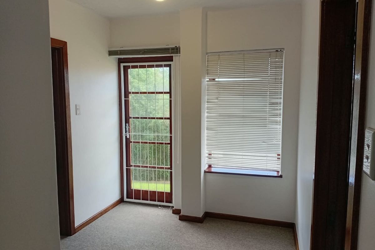 A bright, empty bedroom featuring carpeted flooring, timber door frames, and a security gate leading to the exterior.