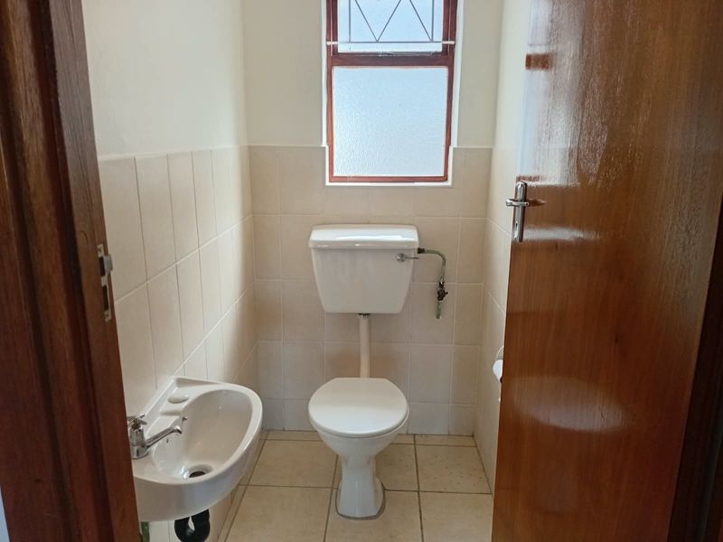 A compact guest bathroom featuring a toilet, wall-mounted basin, tiled walls, and tiled flooring with a window for natural light.