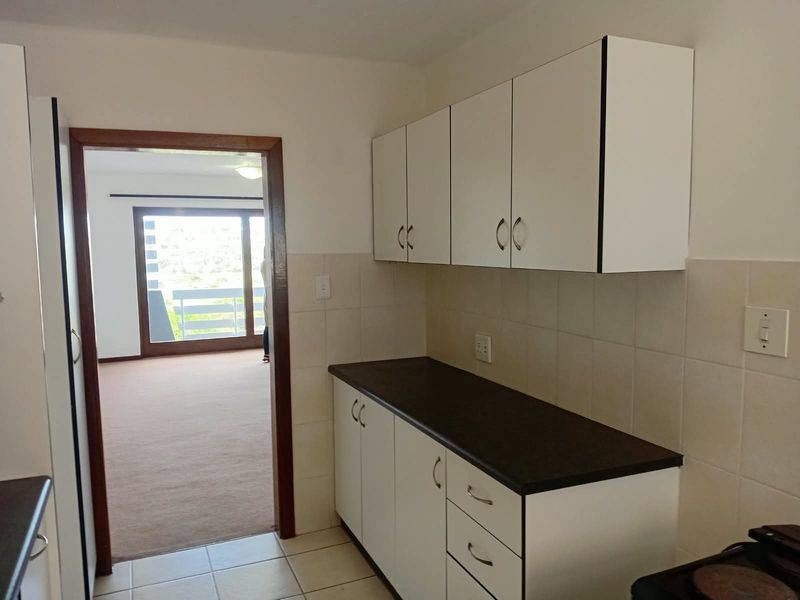 A functional kitchen area featuring white built-in cabinetry, dark laminate countertops, and tiled backsplash, leading into an adjacent living space.