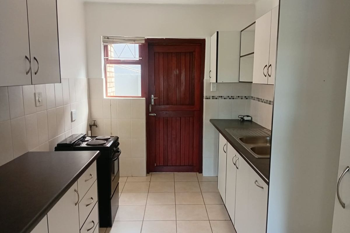 A functional kitchen featuring white cabinetry, dark laminate countertops, a double sink, and a freestanding stove with direct access to the exterior.