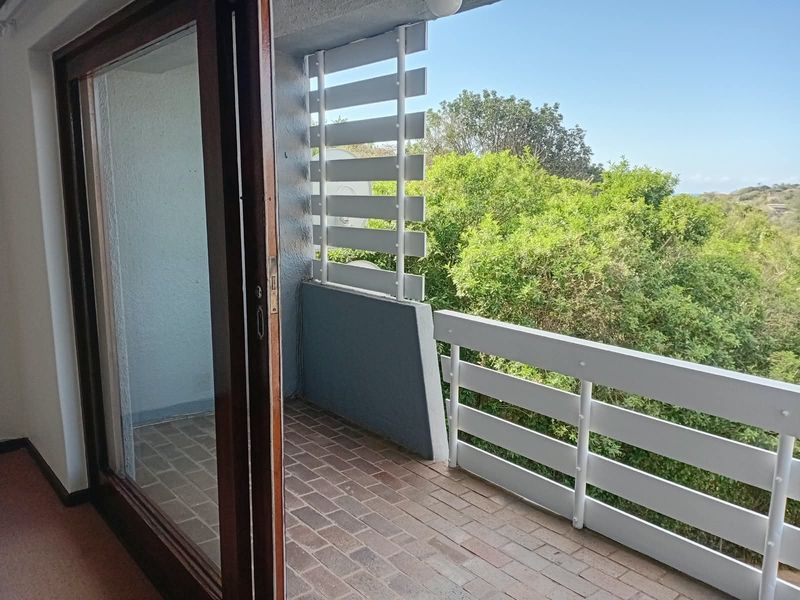 A private balcony featuring brick flooring, a white metal balustrade, and a privacy screen, offering an elevated view of the surrounding greenery.