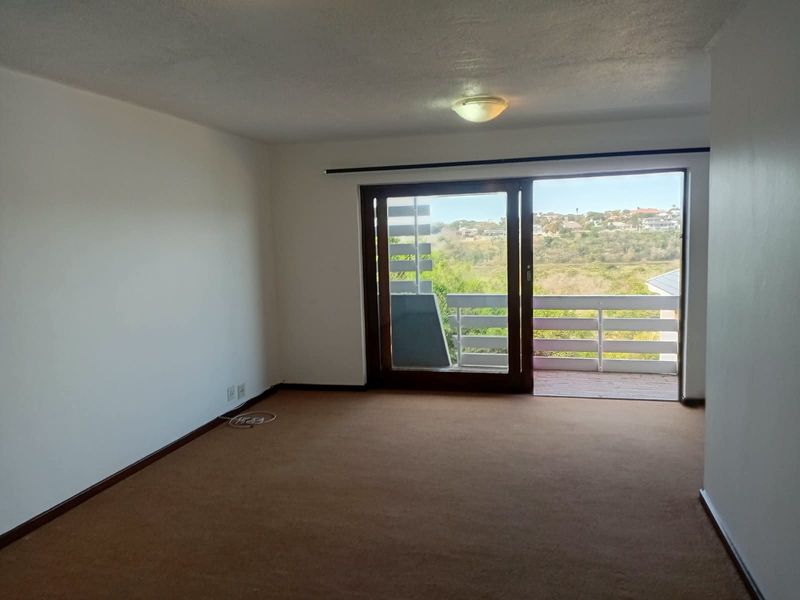 An empty living room featuring carpeted flooring and a sliding glass door that opens onto a balcony with scenic views.