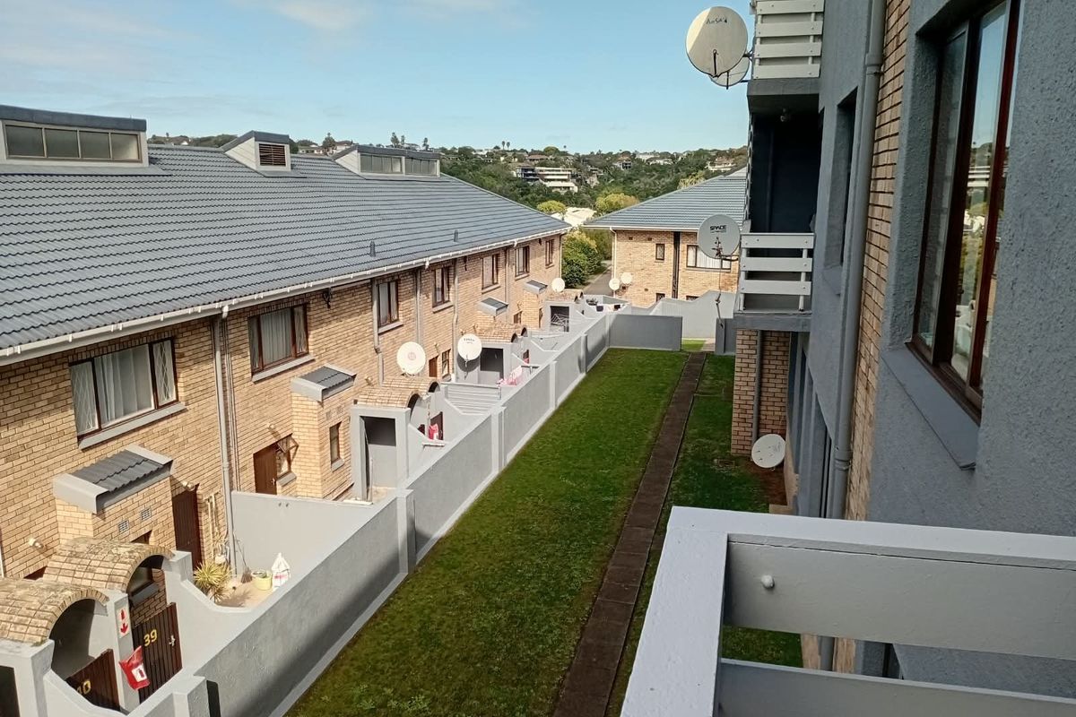 View of the townhouse complex rear exterior, featuring brick facades, tiled roofs, private boundary walls, and a shared garden area.