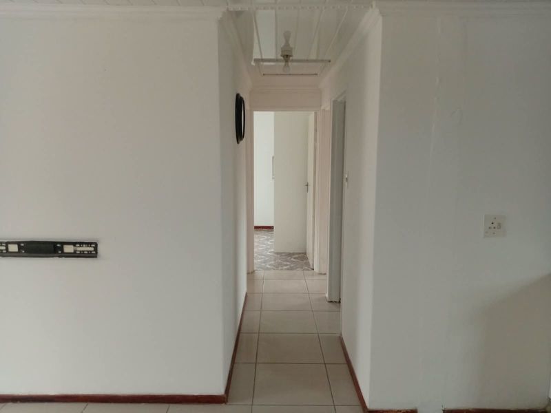 A simple, empty hallway featuring tiled flooring and white walls, providing access to adjacent rooms within the property.