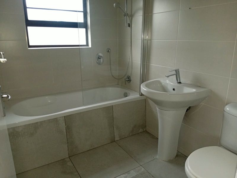 A functional bathroom featuring a pedestal basin, built-in bathtub with a glass shower screen, and neutral ceramic tiling throughout.