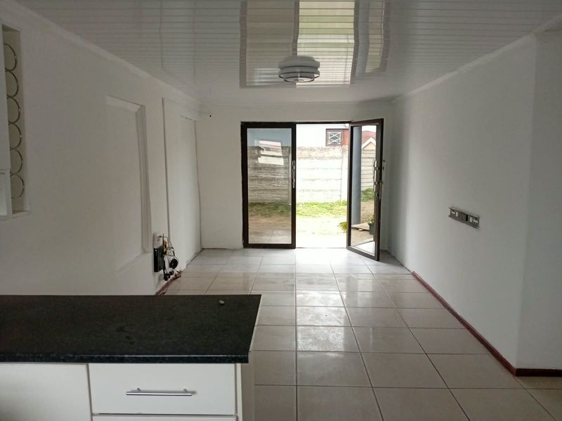 An open-plan living and kitchen area featuring tiled floors, a glossy ceiling, and direct access to the rear garden through double glass doors.
