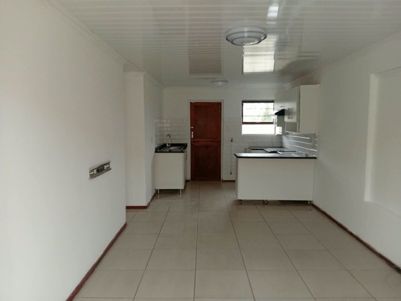 An open-plan kitchen and living area featuring tiled floors, white cabinetry, and a functional kitchen layout in a clean, vacant space.