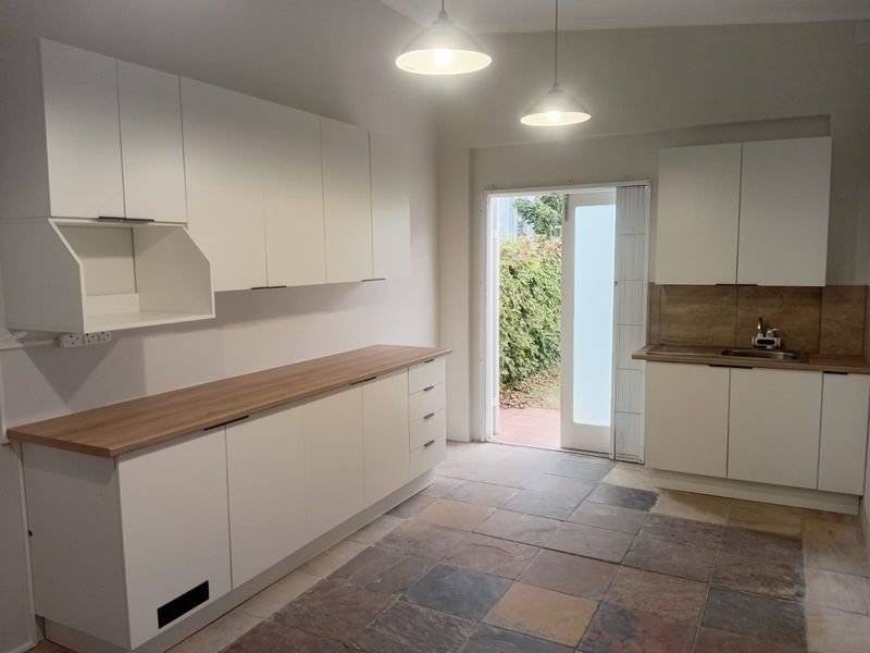A clean, modern kitchen featuring white cabinetry, wood-look countertops, stone tile flooring, and direct access to an outdoor area.