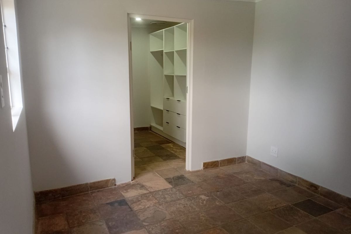 A clean, empty bedroom featuring natural stone tile flooring and a walk-in closet with built-in shelving and drawers.