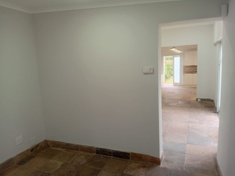 A bright, empty hallway featuring natural stone tile flooring, leading through to an open-plan kitchen area with neutral wall finishes.