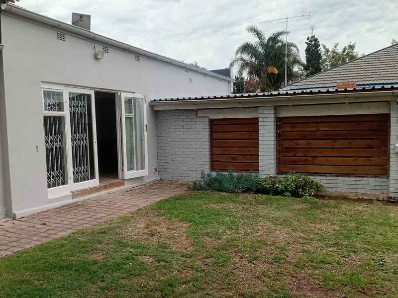 Rear exterior view featuring a paved patio area, security-gated double doors, and a timber privacy screen against a painted brick wall.
