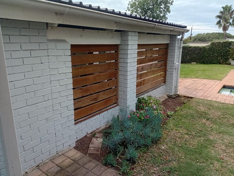 Rear exterior view featuring a painted brick wall with timber slat privacy screens, adjacent to a paved patio area and swimming pool.