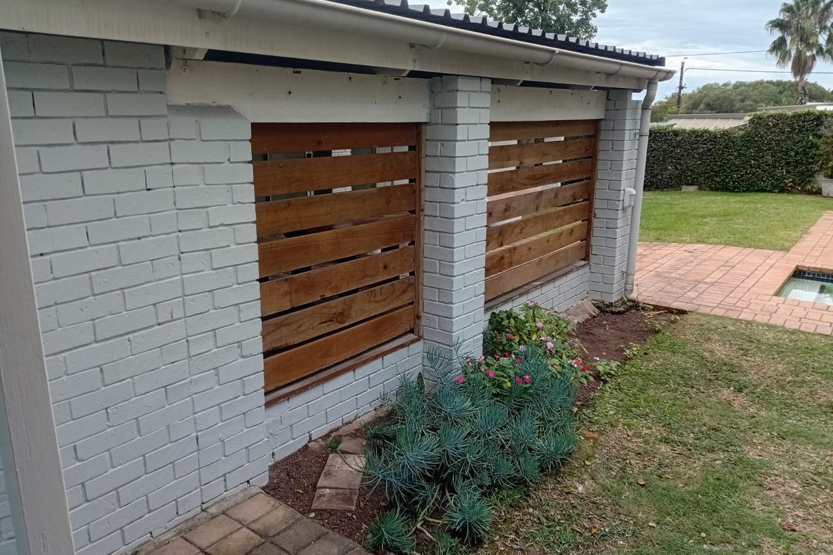 Rear exterior view featuring a painted brick wall with timber slat privacy screens, adjacent to a paved patio area and swimming pool.