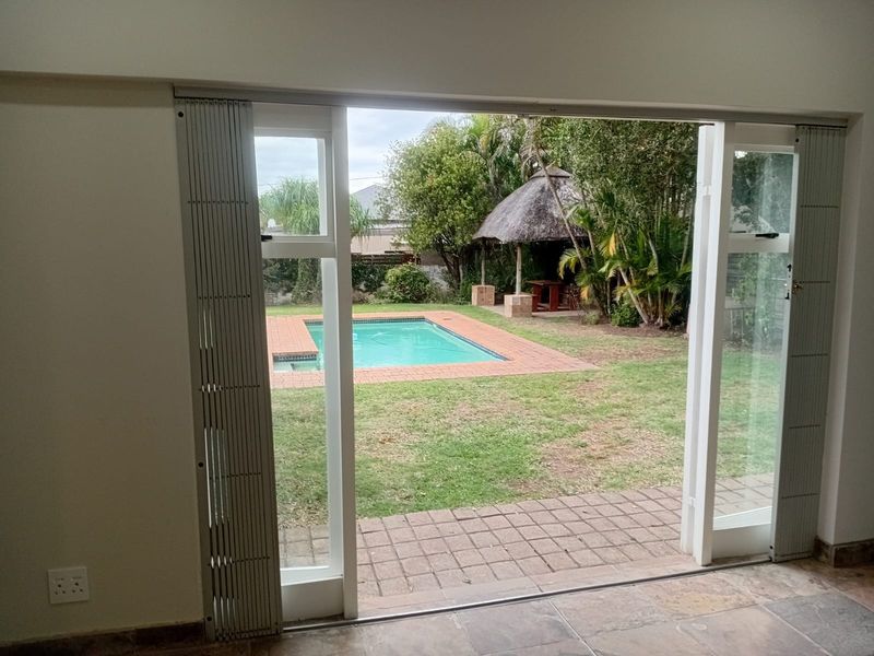 Spacious living area featuring tiled flooring and a large sliding security gate opening onto a private garden with a swimming pool.