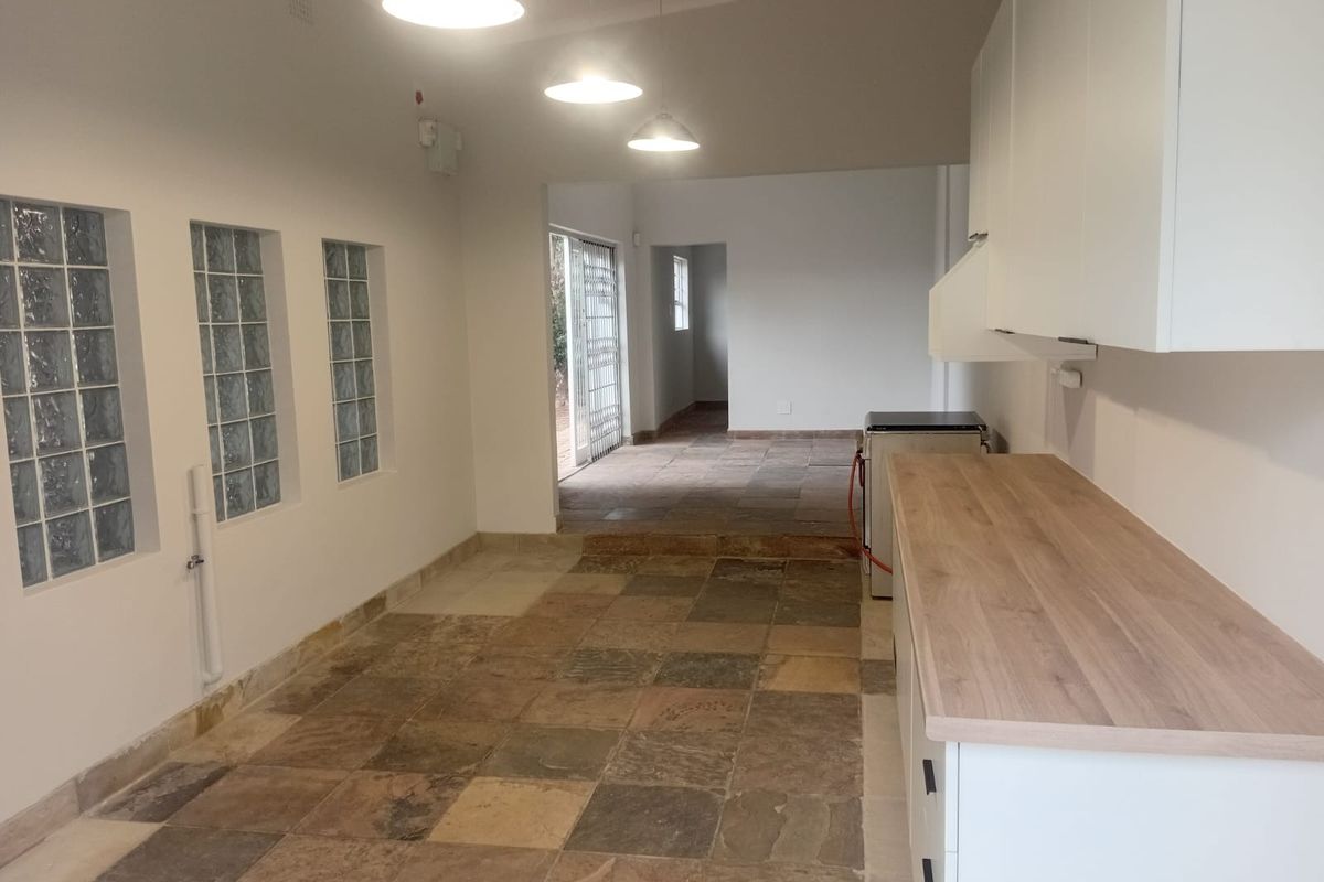 A bright, empty kitchen area featuring stone tile flooring, glass block windows, and modern white cabinetry with a wooden countertop.