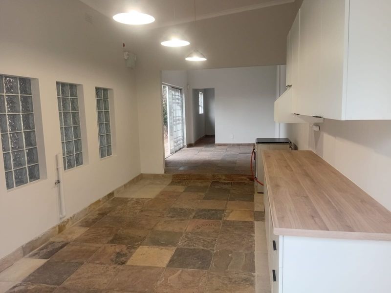 A bright, empty kitchen area featuring stone tile flooring, glass block windows, and modern white cabinetry with a wooden countertop.