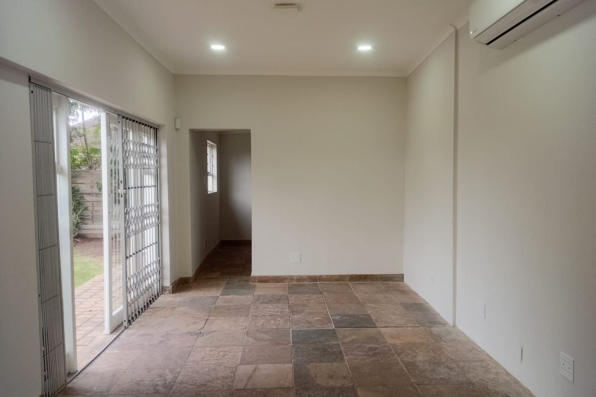 An empty, well-lit living area featuring tiled floors, a split-system air conditioner, and sliding glass doors providing access to the outdoor space.