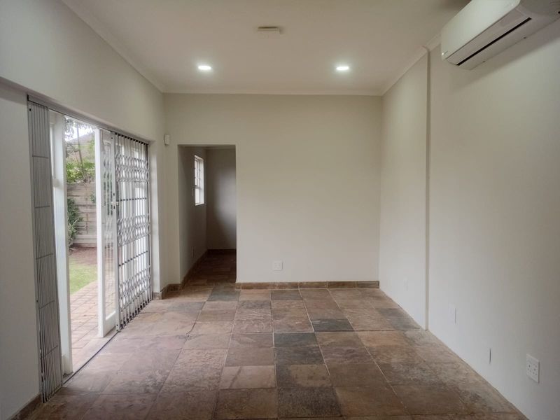 An empty, well-lit living area featuring tiled floors, a split-system air conditioner, and sliding glass doors providing access to the outdoor space.