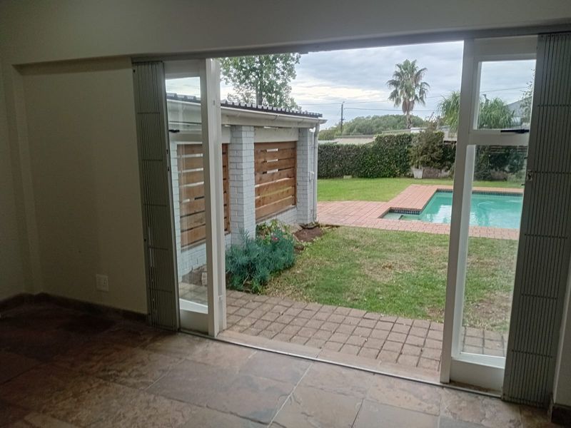 An empty living area featuring large sliding doors that open onto a private garden with a swimming pool and paved patio area.