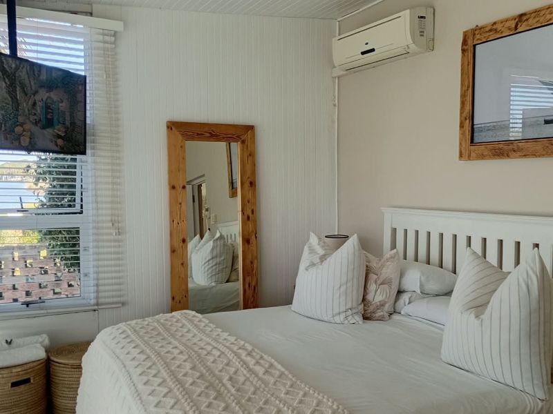 A bright bedroom featuring white timber-look wall paneling, venetian blinds, and a wall-mounted split-system air conditioner.