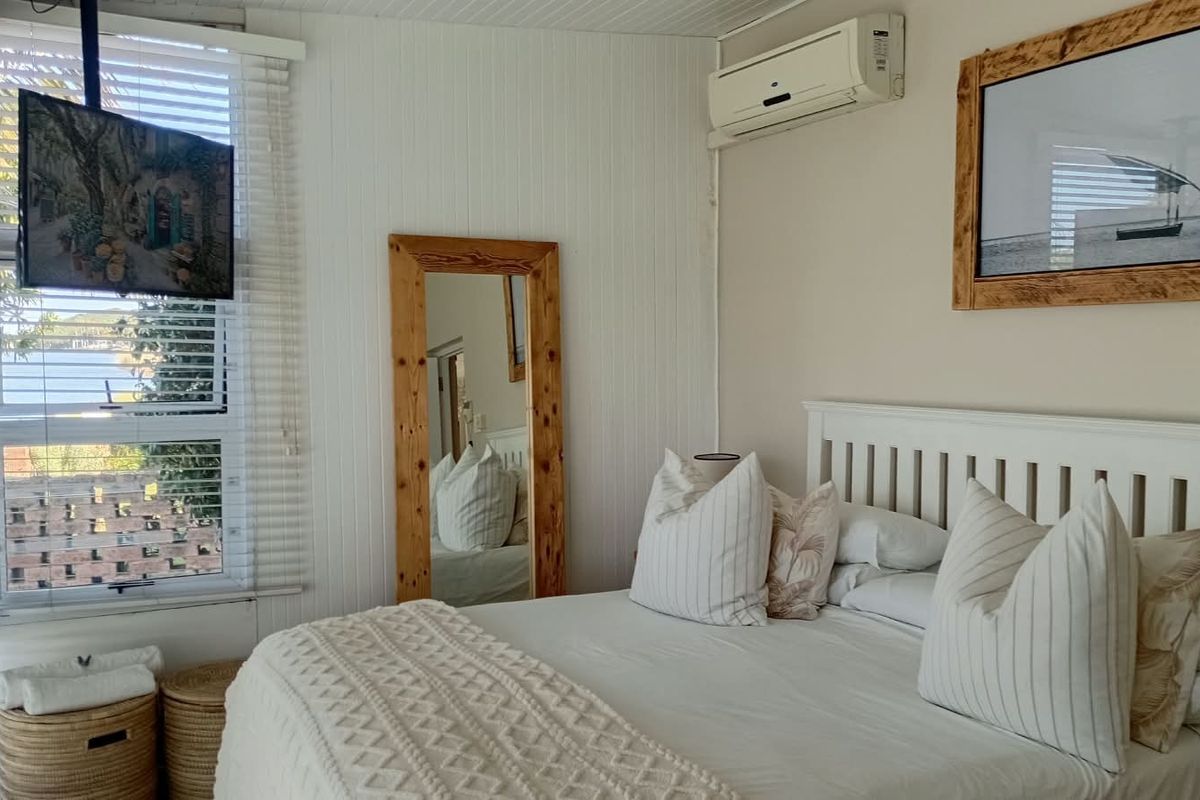A bright bedroom featuring white timber-look wall paneling, venetian blinds, and a wall-mounted split-system air conditioner.