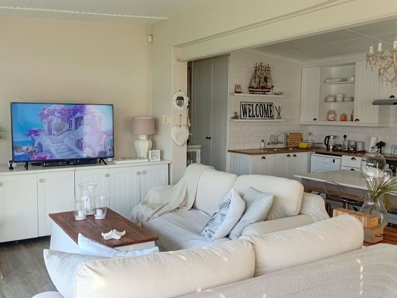 An open-plan living and kitchen area featuring white cabinetry, timber countertops, and a cozy, cottage-style aesthetic with integrated kitchen fixtures.