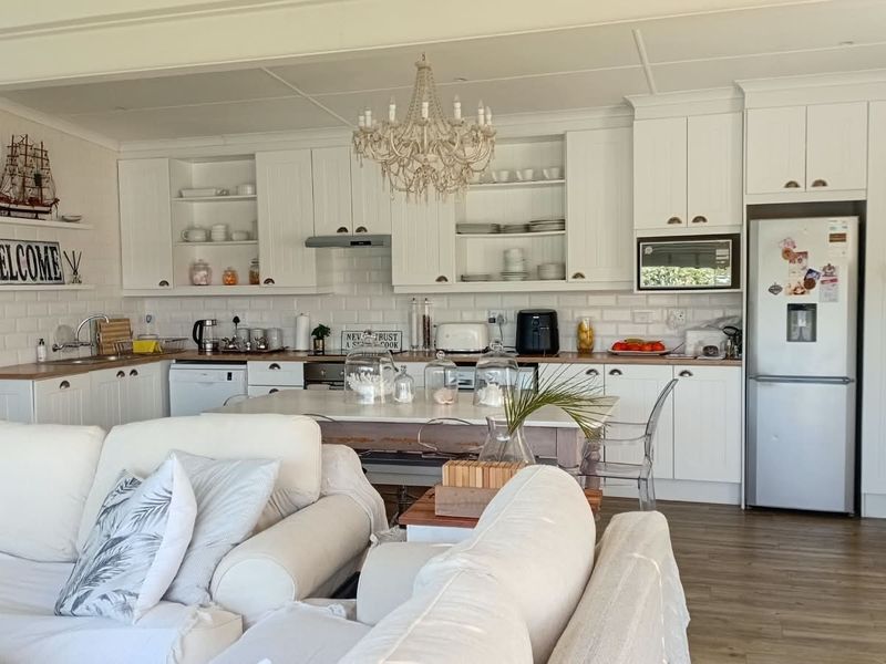 Bright open-plan kitchen featuring white shaker-style cabinetry, timber countertops, subway tile backsplash, and integrated appliances, seamlessly flowing into the living area.