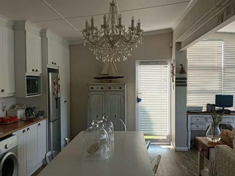 Open-plan kitchen and living area featuring white cabinetry, wooden countertops, and a central chandelier, creating a bright and functional cottage-style living space.