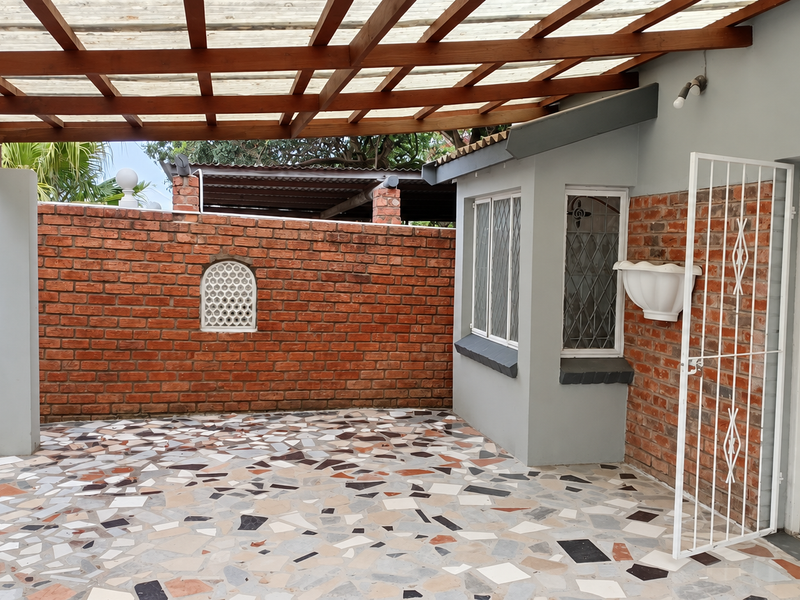 A covered patio area featuring a timber pergola, terrazzo flooring, and exposed brick walls, providing a functional outdoor space with security features.