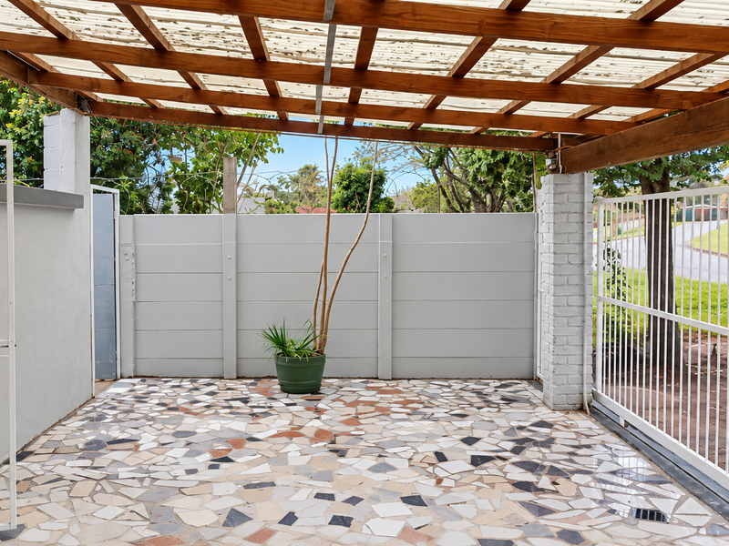 A covered patio area featuring a timber pergola with polycarbonate roofing, crazy paving flooring, and secure gated access.