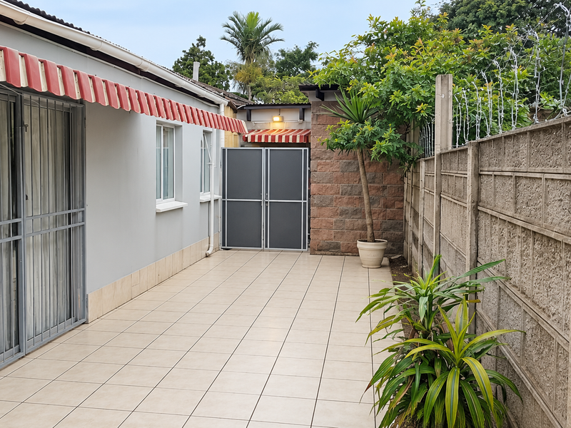 A paved outdoor patio area featuring a retractable awning, secure sliding door access, and a private boundary wall with security fencing.