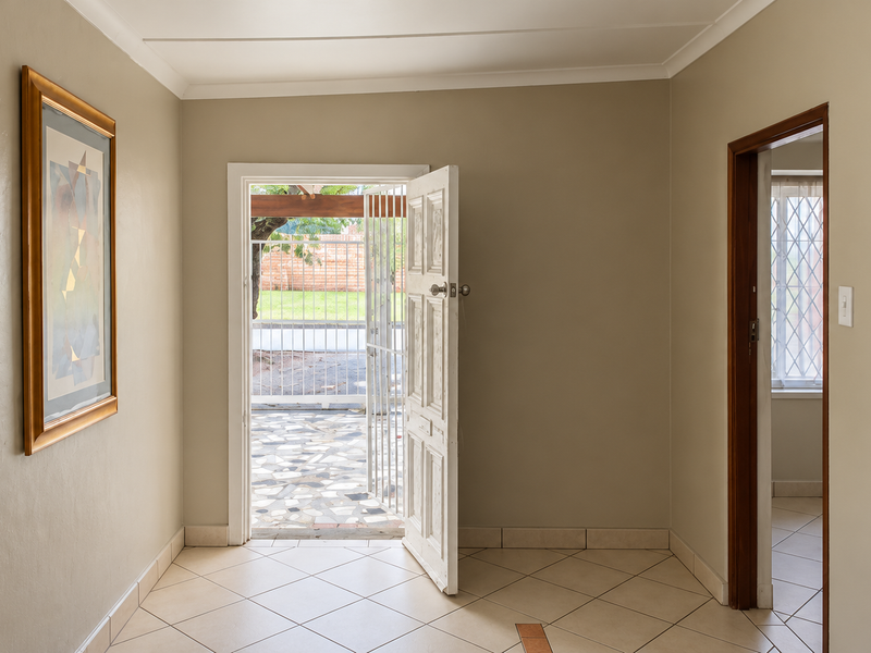 A bright and clean entrance hall featuring tiled flooring, neutral walls, and a secure exterior door leading to a paved outdoor area.