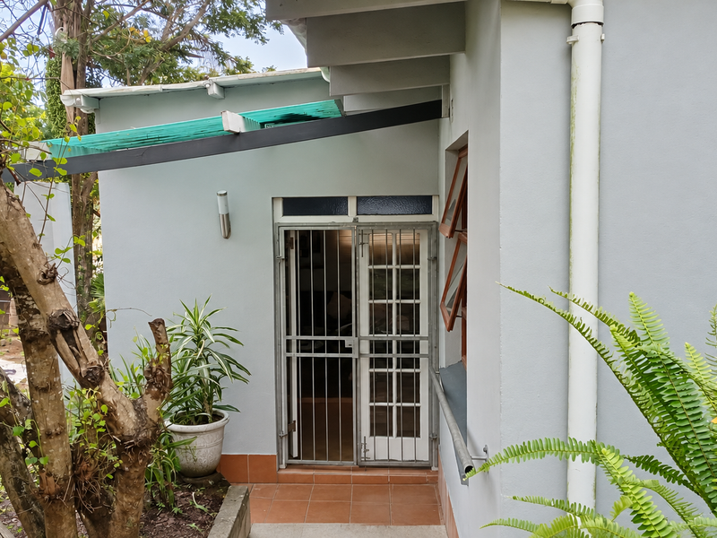 Rear exterior view of the property featuring a tiled patio area, security gate, and functional casement window with an overhead awning.