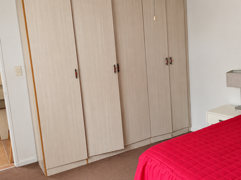 A bedroom featuring light wood-finish built-in wardrobes and carpeted flooring, with a view into an adjacent room.
