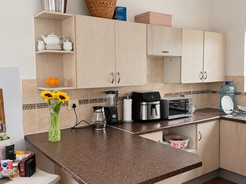 A functional kitchen featuring light wood-tone cabinetry, a dark laminate countertop, and a tiled backsplash with decorative border accents.