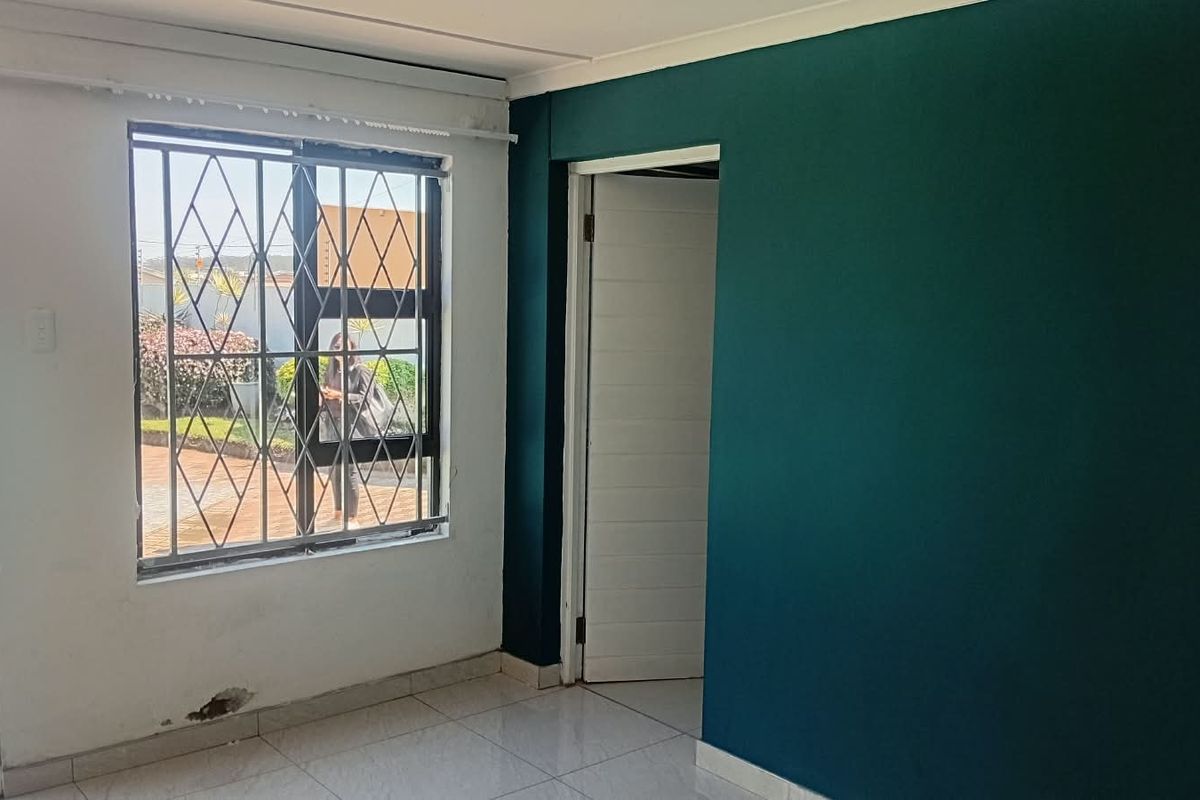 An empty living room featuring tiled flooring, a window with security bars, and a painted accent wall.