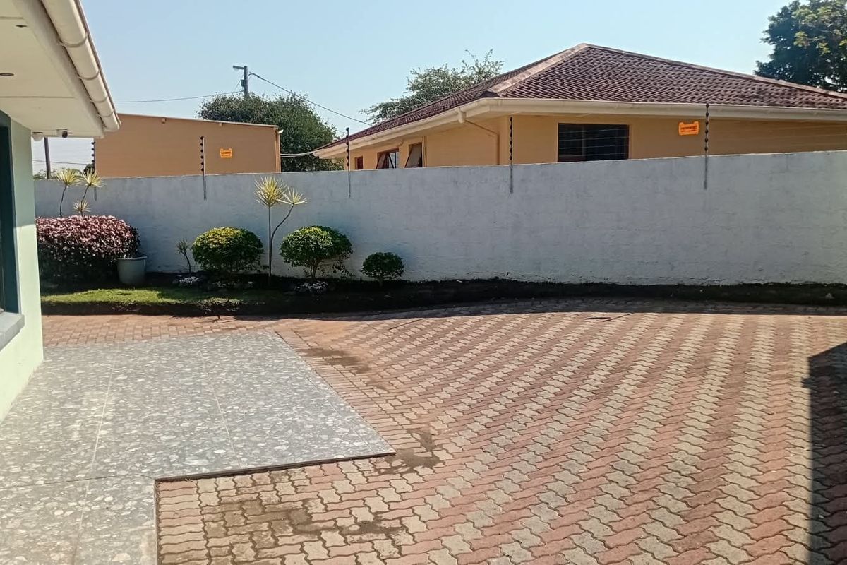 A rear exterior view featuring a paved driveway, a tiled patio section, and a perimeter wall secured with electric fencing.