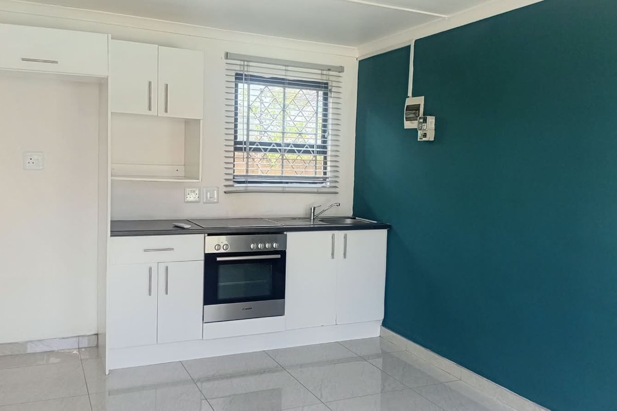 A clean, modern kitchen featuring white cabinetry, built-in oven and hob, stainless steel sink, and tiled flooring with a contrasting teal accent wall.