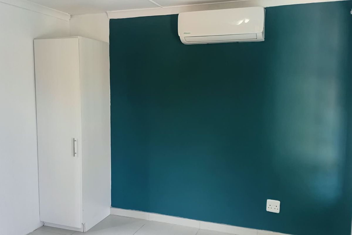 A clean, empty bedroom featuring tiled floors, a built-in cupboard, and a wall-mounted split-system air conditioner against a teal accent wall.