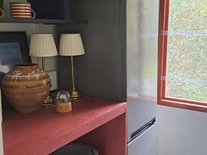 A compact scullery or utility area featuring built-in red cabinetry, open shelving, and tiled flooring, providing functional storage space.