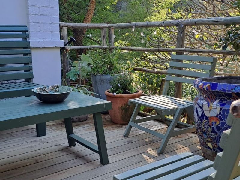 A rustic outdoor timber deck patio featuring a natural wood railing and views of the surrounding garden greenery.