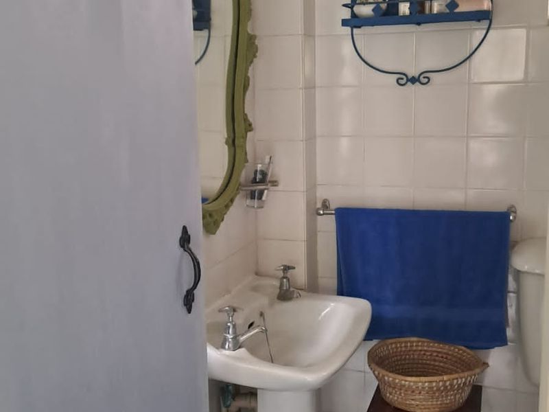 A compact bathroom featuring a pedestal sink, ceramic wall tiling, and dark slate flooring, requiring some cosmetic updates to improve its overall condition.