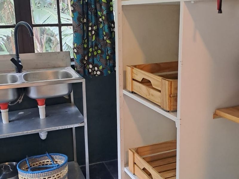 A functional scullery area featuring a stainless steel double sink, black faucet, slate flooring, and built-in white shelving for storage.