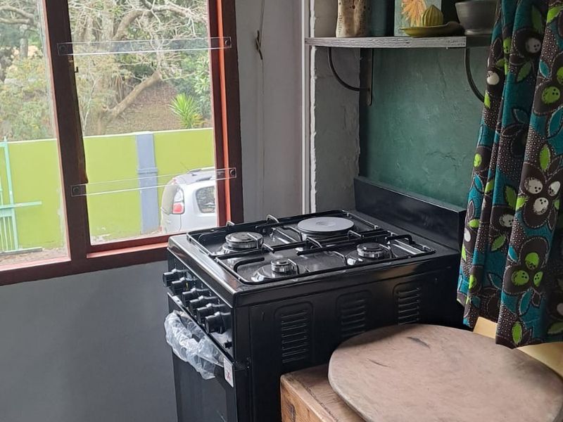 A compact kitchen area featuring a black gas stove, extractor fan, and timber window frame overlooking the exterior.