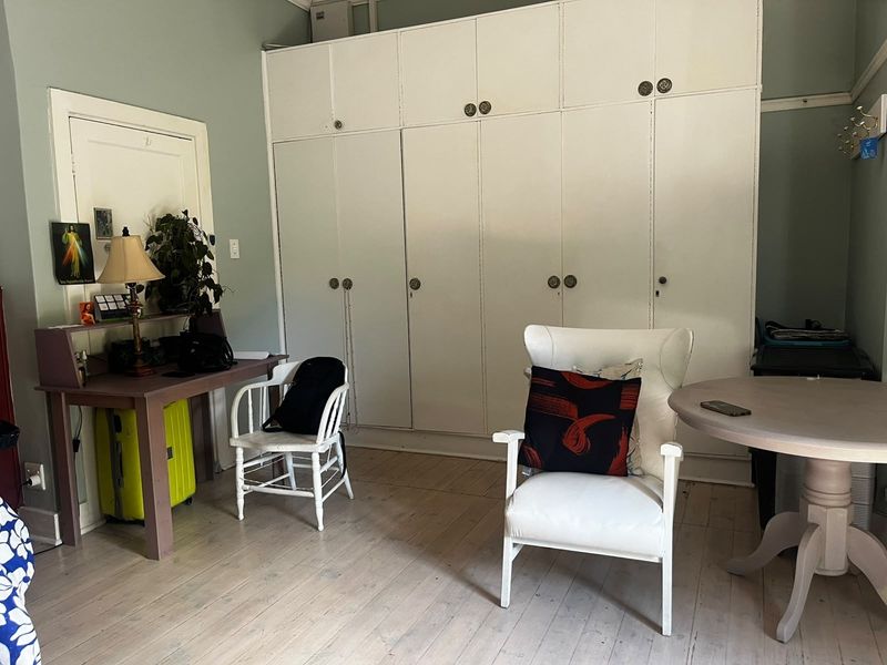 A bedroom featuring extensive built-in floor-to-ceiling storage cupboards and original timber flooring, offering a functional space with potential for cosmetic updates.