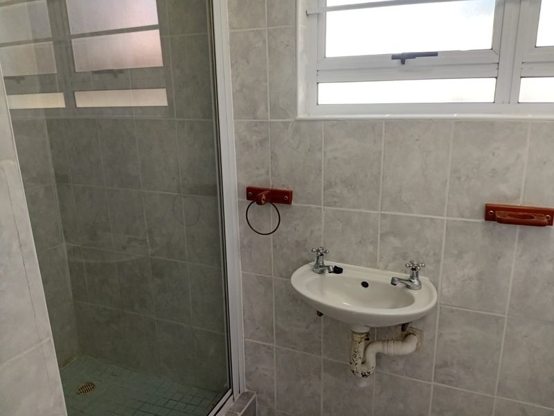 A compact bathroom featuring a shower enclosure and a wall-mounted basin with tiled finishes throughout.